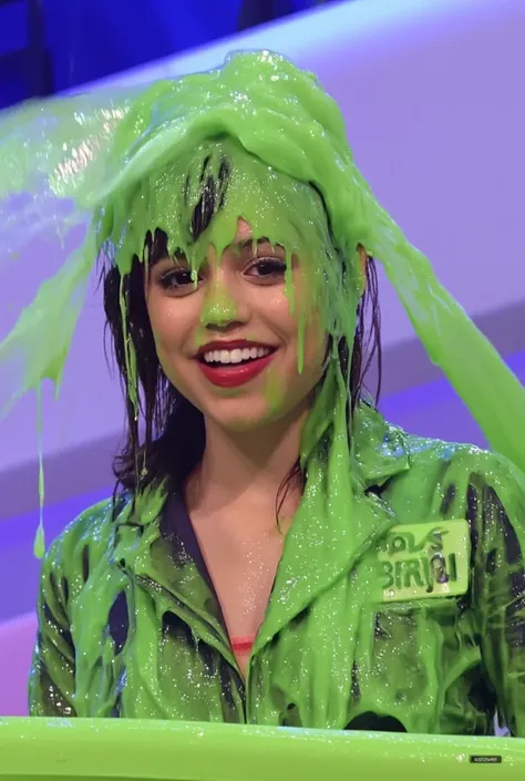 DSLR photograph of an Jenna ortega with short wavy black hair and light skin in a brightly lit game show studio, covered in thick, dripping green water. She wears a black leather bra, which is partially visible beneath the slime. She has long fake eyelashe...