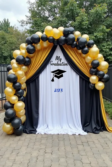 A festive graduation backdrop decorated with an arch made of balloons in black, white, and gold colors. The backdrop consists of black and white drapery with golden fabric accents, elegantly arranged. In the center, the text 'My Graduation 2023' is display...