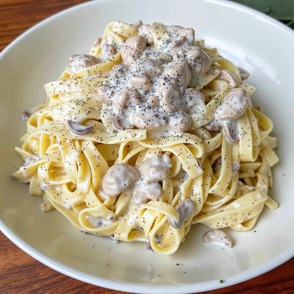 creamy chicken and mushroom pasta, with fettuccine coated in a rich Parmesan sauce, tender chicken slices, and sautéed mushrooms, garnished with fresh parsley and Parmesan.