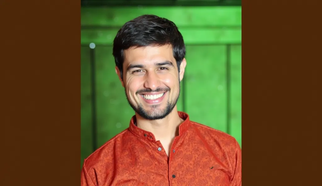 "A vibrant kitchen background with a professional cooking setup. In the foreground, YouTuber Dhruv Rathee is dressed as a chef, wearing a white cook’s dress and a chef’s cap. He is holding a large spoon in one hand and a packet labeled 'Secret Masala' in t...