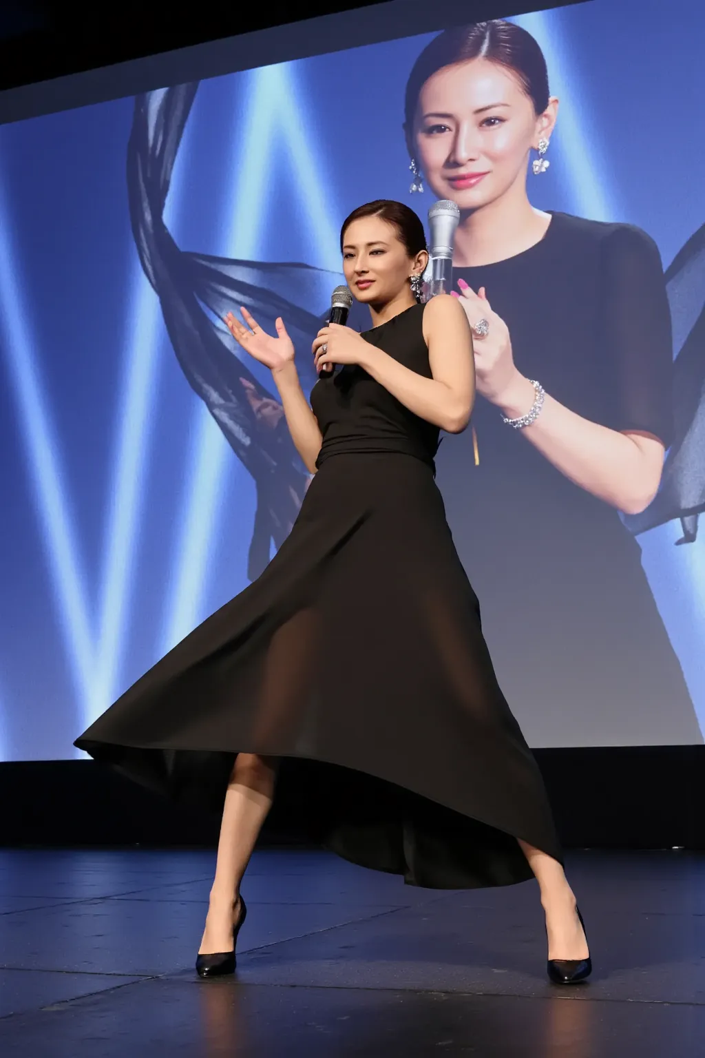 Hi-res photo of a beautiful Japanese woman, she is standing on a movie theater stage with her legs spread out, and masturbating while talking with a microphone,It's a mixture of ,images of her indecent sexual acts are projected onto a large monitor,big bre...