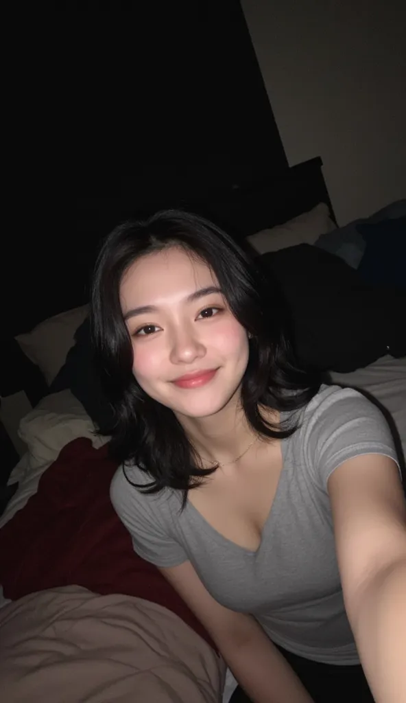 Amateur shot a pov of a instagram selfie. A woman with tshirt off shoulder  surrounded by cushions in a dimly lit student room, no makeup, playful grin. She has medium long and medium curl black hair, her pale skin contrasting against the dark bedding.