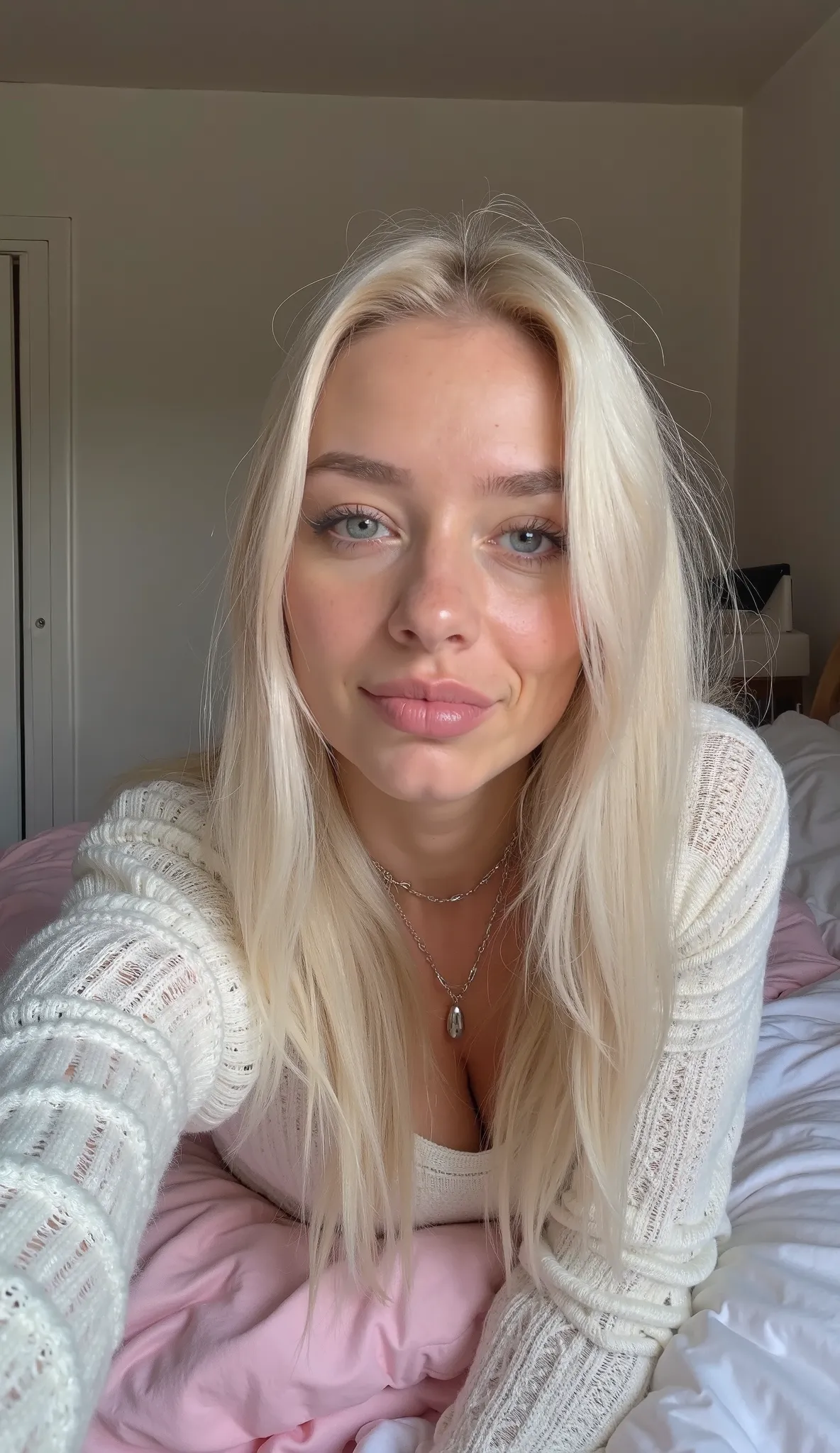 Create image of TaissaFarmig, 26 years old, round face, light textured skin, long, straight platinum blonde hair, moisturized hair, clear lip gloss, natural blue eyes, upturned nose. Wearing a semi-sheer white sweater. She is lying on her stomach on a whit...