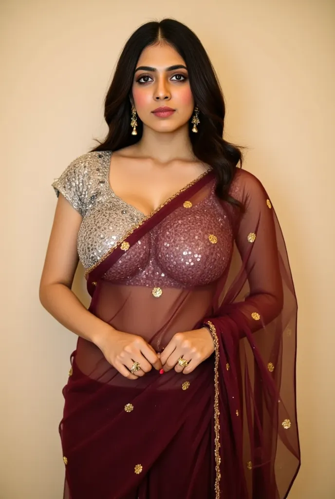 A woman, of South Asian ethnicity and appears to be in her 20s or 30s, is the central subject.  She is positioned slightly off-center to the left of the frame.  She is wearing a deep burgundy, sheer saree with gold sequin embellishments, flowing over her b...