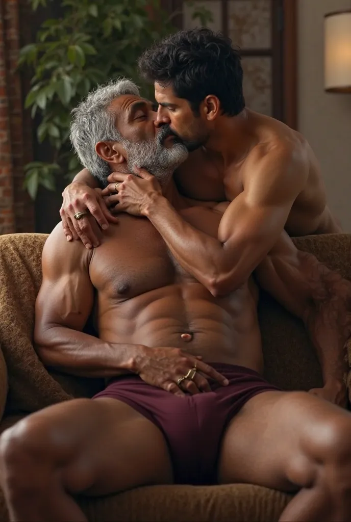 A Matured muscular hot indian man with grey hair wearing a maroon underwear sitting on sofa spreading legs. A young indian shirtless man from behind the sofa kissing the matured man passionately 