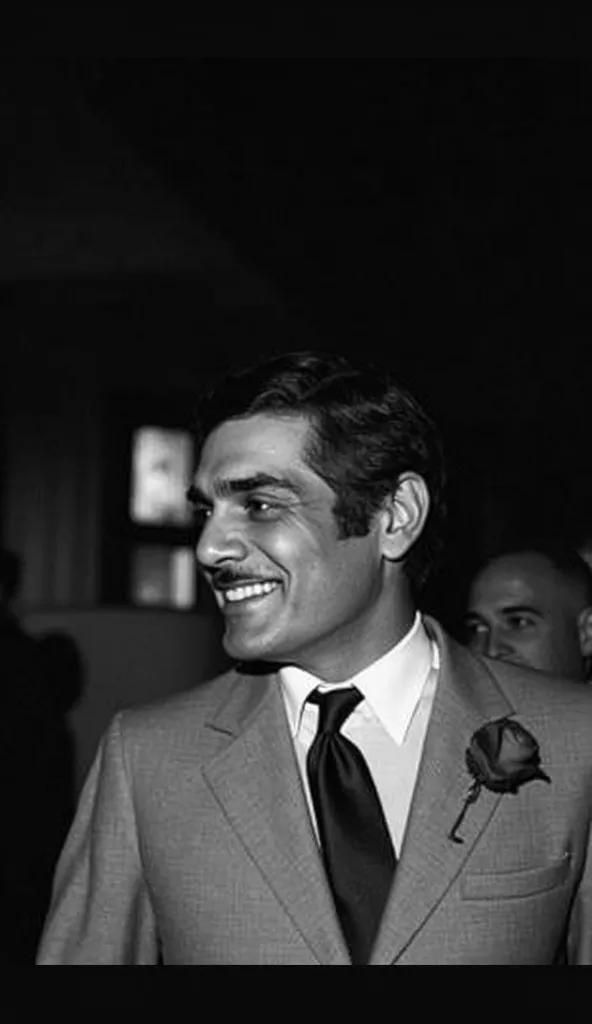 A hyper-realistic black and white cinematic portrait of a charismatic Middle Eastern man in a vintage 1960s suit, with a classic tie and a rose on his lapel. He has a confident smile, sharp facial features, and neatly styled hair. The lighting is dramatic ...