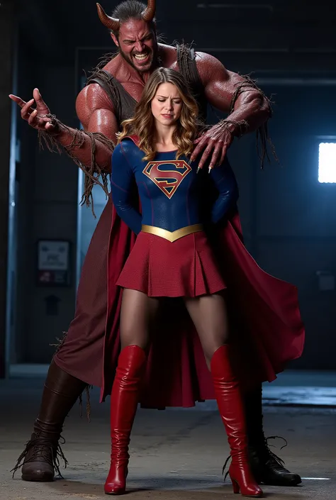 Melissa Benoist as Supergirl, she is screaming in pain, arms behind her back, try to resist, wearing a Supergirl costume, blue shirt and very short skirt, red high boots, she is harassed from behind by a huge body devil, A fierce devil is holding her arms ...