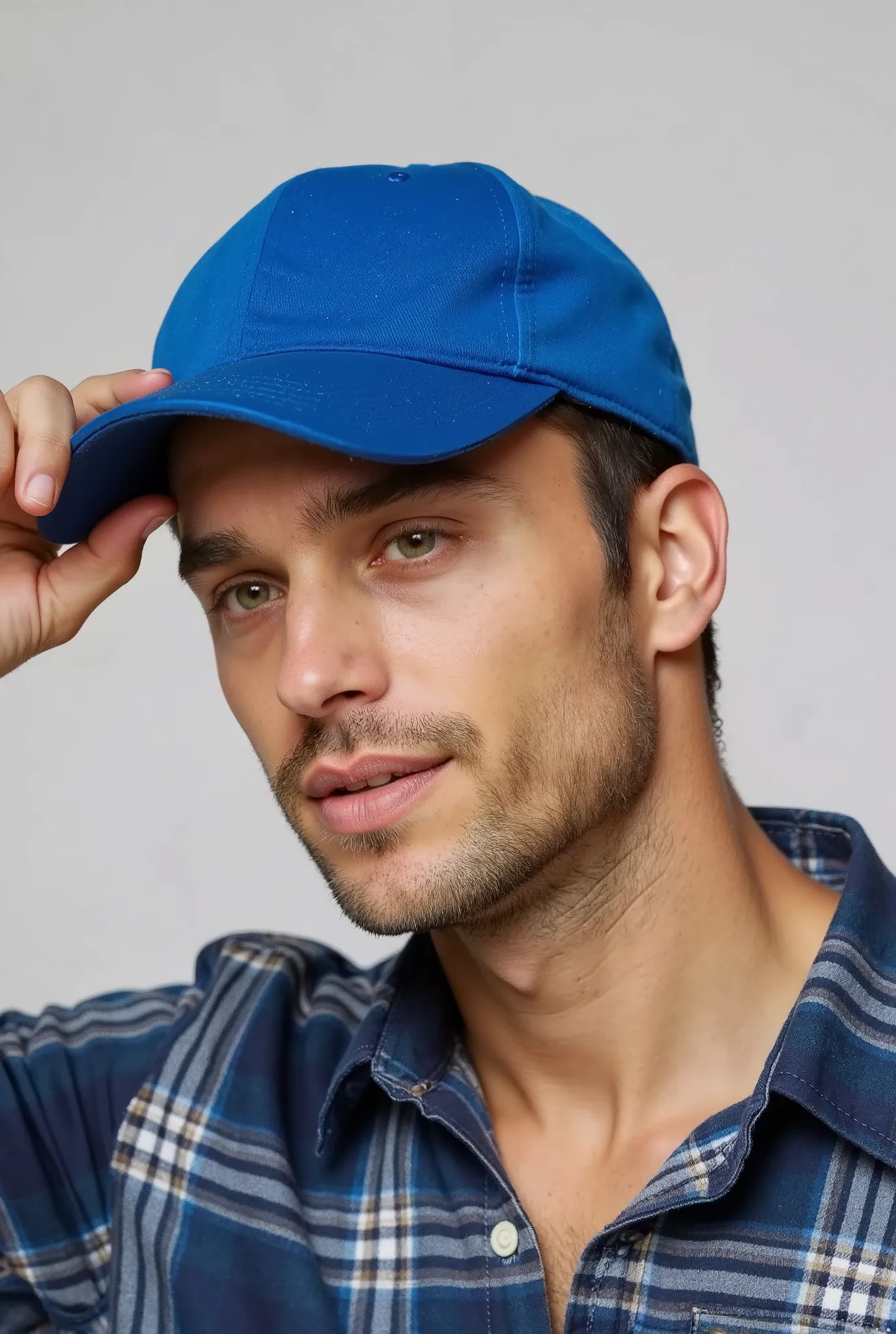 Close-up of a man wearing a simple blue cap and a plaid shirt, tilting the head slightly downward, while holding the cap brim with one hand. The background is simple and light gray . Your expression is relaxed and subtle, and his face is partially obscure...