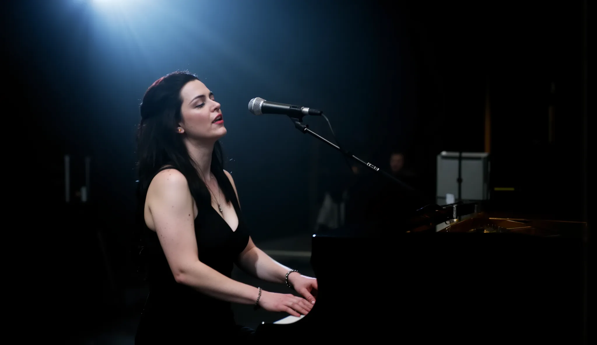 Amy Lee from Evanescence, wearing an elegant black dress with a deep neckline, playing the piano passionately while singing, dramatic gothic atmosphere, soft spotlight highlighting her face, dark background with subtle fog, emotional intensity in her expre...