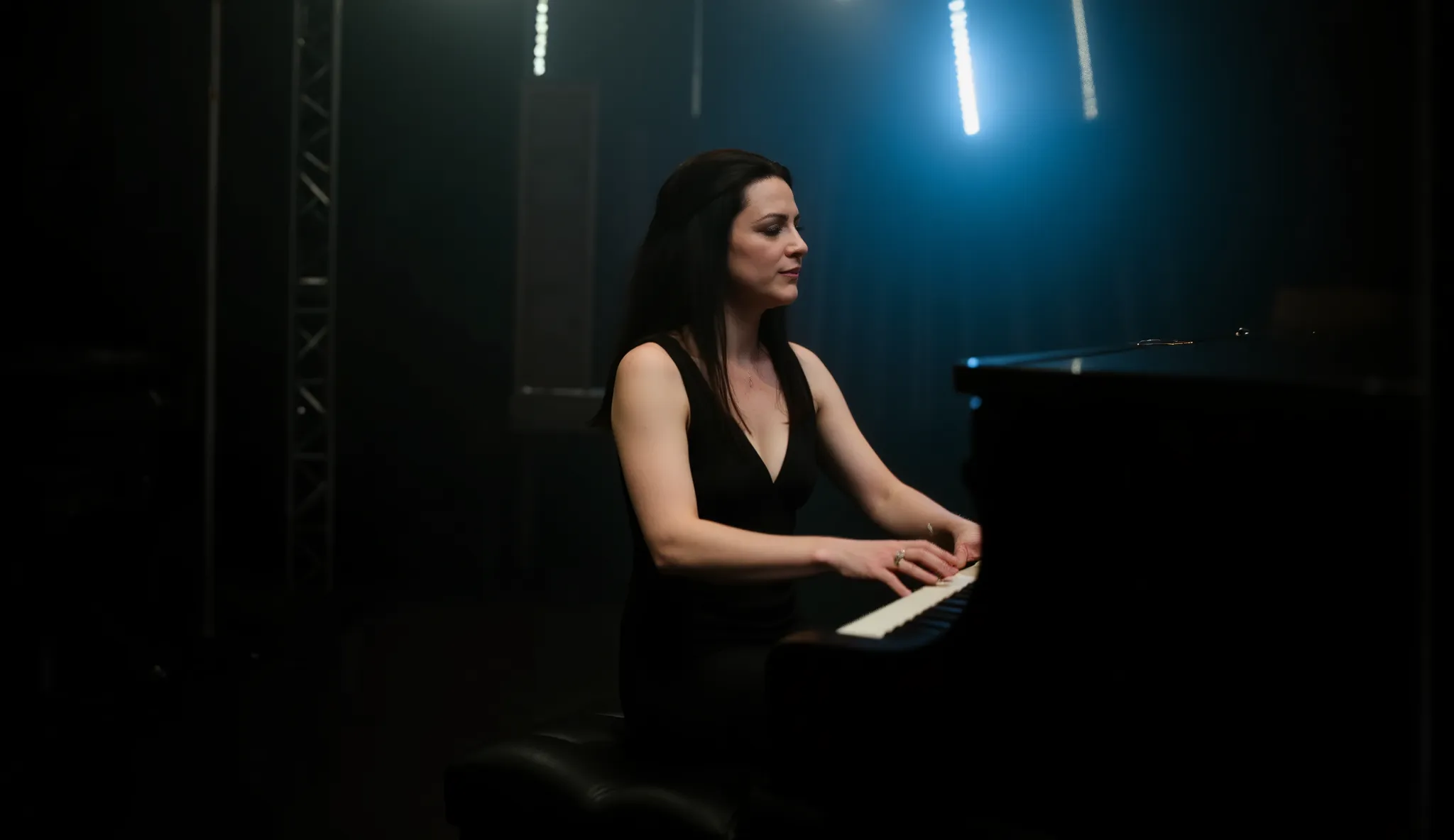Amy Lee from Evanescence, wearing an elegant black dress with a deep neckline, playing the piano passionately while singing, dramatic gothic atmosphere, soft spotlight highlighting her face, dark background with subtle fog, emotional intensity in her expre...