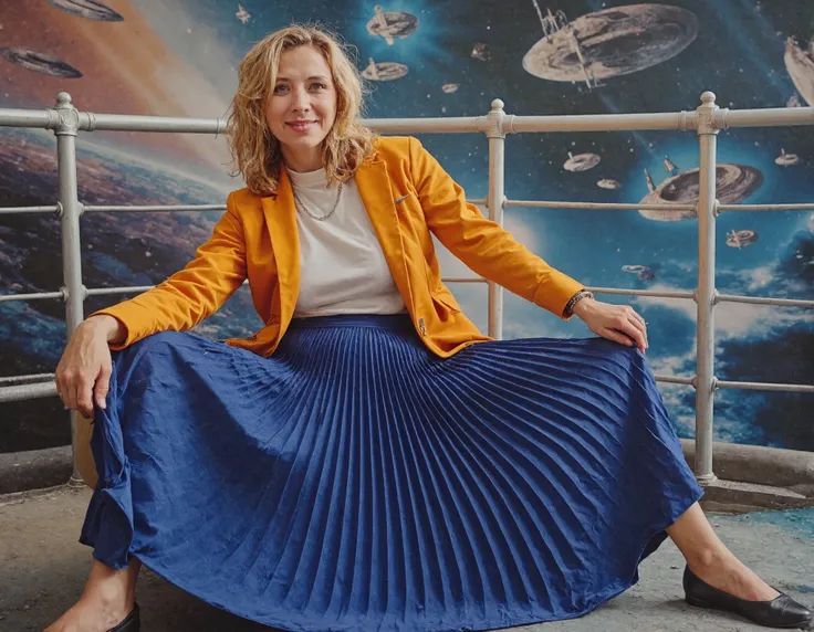 A stunning portrait captures my mother's mature beauty as she sits confidently on top of her desk, daringly spreading her legs amidst a vibrant space station backdrop featuring galaxies and spaceships. Her long pleated skirt flows around her, juxtaposing ...