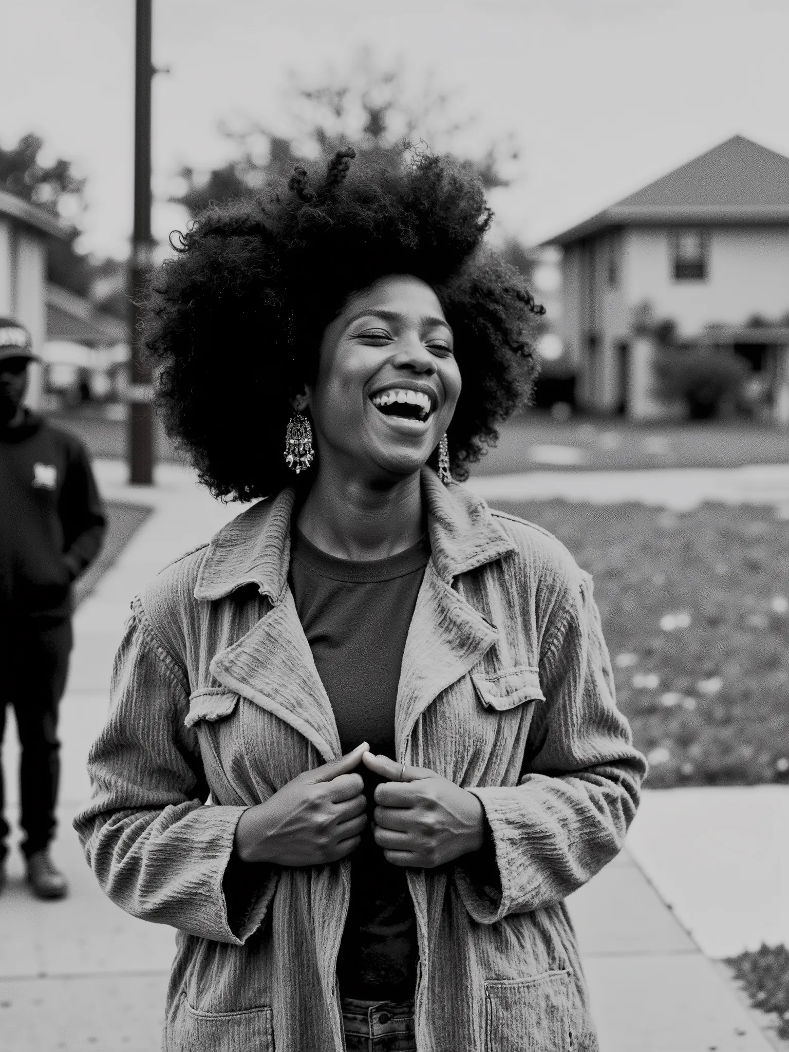 Ultra-realistic black and white photograph of a joyful woman laughing heartily in an outdoor urban neighborhood setting. She has a voluminous curly afro hairstyle and wears large, ornate chandelier earrings. Her expression is full of life and energy, mouth...