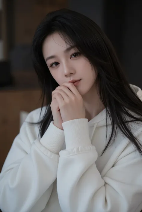 A young woman with long, straight, and silky jet-black hair flowing gently over her shoulders and chest, wearing an oversized white hoodie with the sleeves partially covering her hands. She poses indoors against a faintly blurred backdrop of dark wooden wa...
