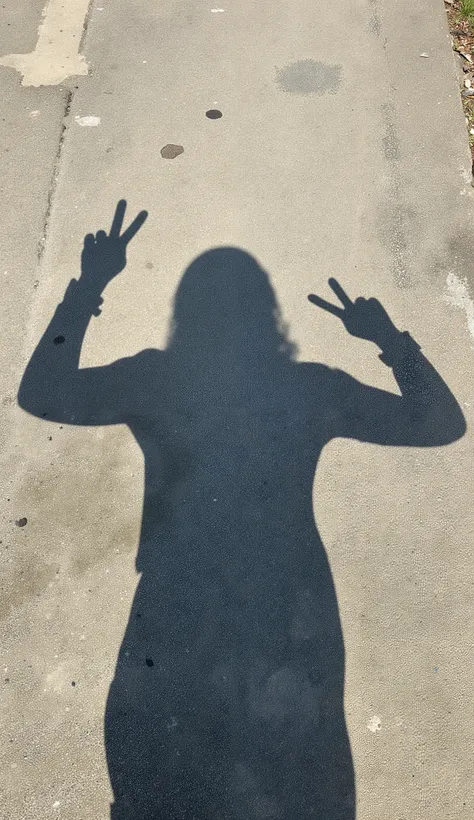 The image shows shadows of people reflected on a textured concrete surface, judging from the clear scenery on a clear day, defined contours. The shadow silhouette suggests someone with long hair, The outline of the head and shoulders clearly stand out. I'm...