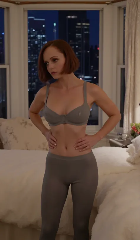In a bedroom, full body shot of Christina Ricci with dark red hair standing beside a bed with her feet on the floor. she is facing the viewer turned slightly to the side. she is wearing a gray rubber bra and tight fitting gray rubber tights, getting dress...