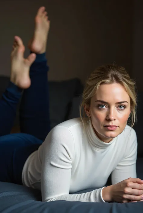 Actress Emily Blunt laying on her stomach doing the pose with her feet kicked up, she is wearing dark blue velour plush leggings and a white turtleneck that accentuate her curvaceous figure