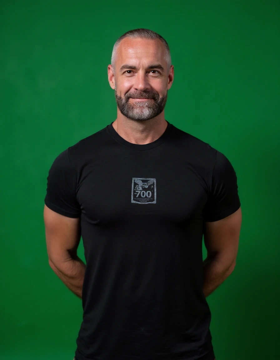 j@yh@rr1ng70n This is a photograph of a handsome, muscular man standing in front of a green background. He is bald with a beard. He is wearing a black t shirt with a graphic on it that says "F000". He is looking at you. He has a smile on his face. Depth of...