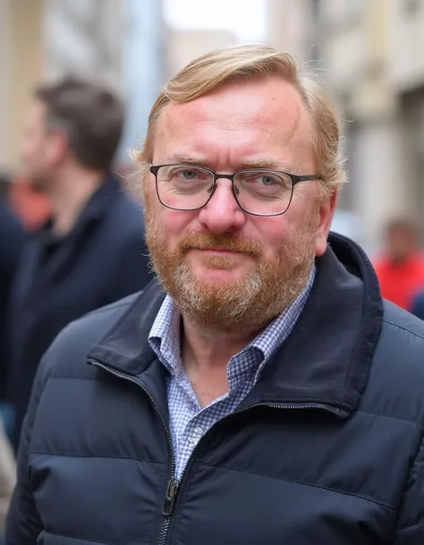 The image shows a 50 years old man posing at the street. He has a beard and glasses and is looking directly at the camera with a serious expression on his face. Behind him,there are other people.