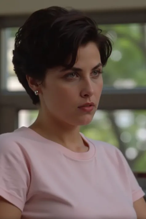 A close-up shot of a woman with short dark brown hair, wearing a light pink t-shirt, is seen from the waist up. She is looking off to the right, with a serious expression on her face. The background is blurred, with greenery visible in the window behind he...