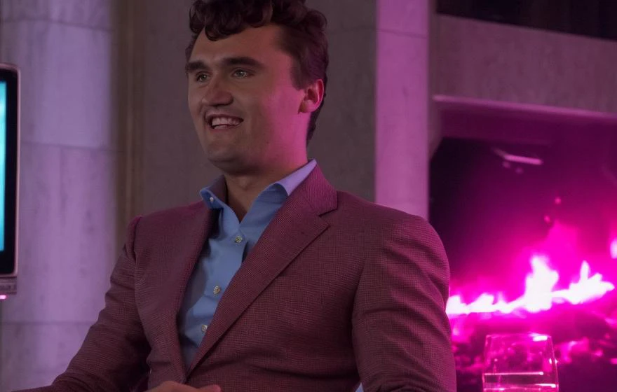 movie film still of charliekirk person wearing a pink leather bodysuit in the lobby of the fancy trump tower NYC by guest registry, high on cocaine, shocked awed facial expression, holding his laptop with the power cord dangling.