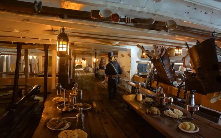 wooden planks, gun deck, cannons, mess table, below deck, ((pirate crew eats dinner), pirate men, eating, banquet, biscuits, meat, ale,)