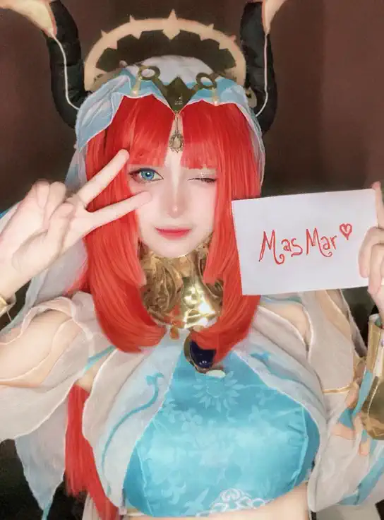 A cute anime-style girl with bright red hair and blue eyes, wearing an elegant fantasy costume with gold accents and a horned headdress, gently kissing a small white sign she's holding with both hands. Her eyes are softly closed, her lips touching the sign with a tender expression, as if sending a kiss to someone special. The atmosphere is sweet and warm, with soft lighting that highlights her gentle smile and natural charm. The text “MasMar ♡” is still clearly visible on the sign. Focus on making the scene feel adorable and heartfelt.