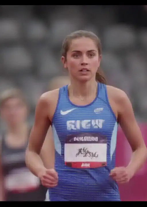 young woman. She's a running athlete. She's getting ready to start running at the start. Nearby, other athletes are also preparing for the start. She's wearing an athlete's running uniform. full stands. day. bright light.