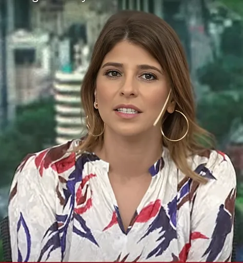 Uma mulher 30 anos, cabelos longos castanho, olhos castanhos bem delineados olhando para a foto, sorrindo, de camisa floral e brincos de argola no Today Show, rosto detalhado, planos de fundo detalhados pouco desfocados, luzes naturais, HDR, foto realista,...