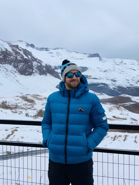 arafed man in blue jacket and hat standing on a snowy hill, with mountains in the background, with mountains in background, with...