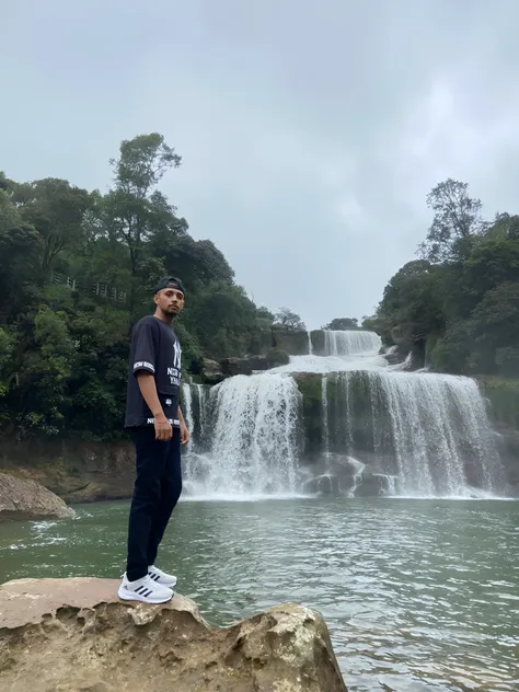 arafed man standing on a rock in front of a waterfall, waterfalls in the background, waterfall in the background, standing in front of a waterfall, with a waterfalls, standing near a waterfall, next to a waterfall, with waterfalls, waterfall in background,...