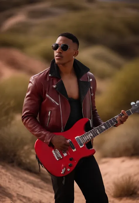 Still American SHOT of a young African-American mestizo mixed-race man wearing red round sunglasses wears a shirtless leather jacket where his abs are seen with a Fender Stratocaster guitar in a desert walking with a red scarf with white dots looking at a ...