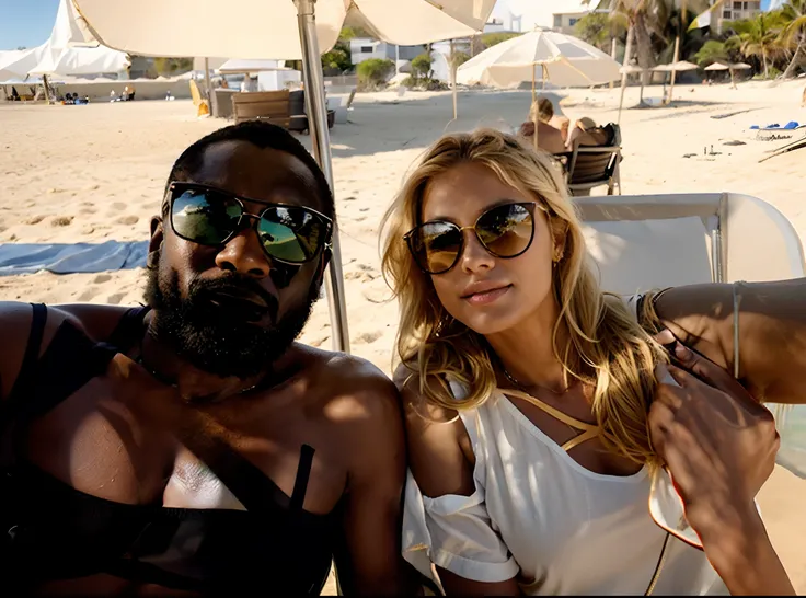 A couple on the beach in sunglasses, The man is black and the woman is blonde.