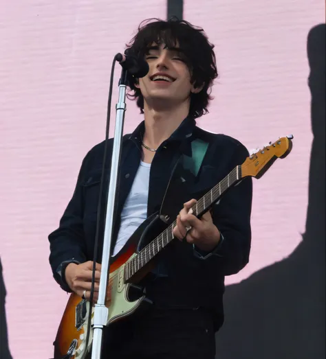 Araffe man with a guitar and a microphone in front of a pink wall., Nick Drnaso, Declan McKenna, Finn Wolfhard, Templos, Miles Johnstone, Ed OBrien (guitarra), Tocar la guitarrara en el escenario, Greg Rutowski, Marco Lense, Realizar, Jonny Greenwood (Guit...