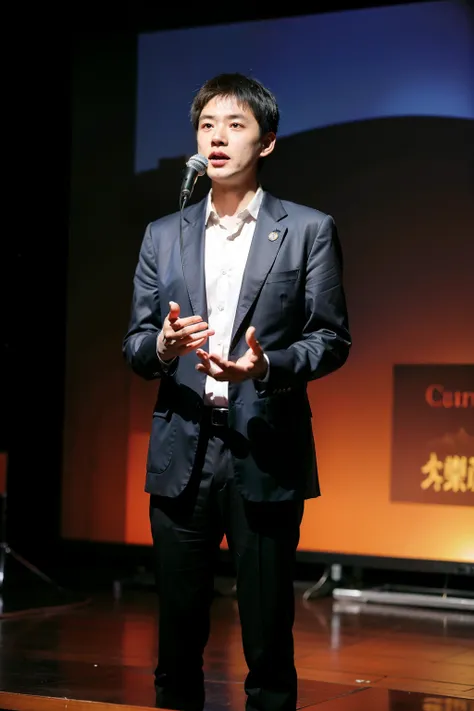 Zhang Yanlong, associate professor at Peking University Guanghua School of Management，male people，holding a mic，are standing，There  a big screen in the back，The suit  straight，Very bookish，spotlight lights