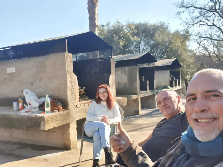 Hay tres personas sentadas afuera de un edificio con chimenea., con unas salchichas al fuego, having a great time, with big birds, mirando orgulloso, Having a good time, Divertirse bajo el sol, good lighting in the afternoon, real picture taken in zoo, Lug...