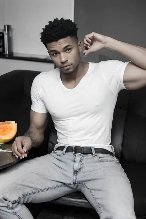 un homme musclé portant un tee-shirt noir et un jean blanc de couleur antillaise , assis sur une chaise à table. sur la table il y a un panier de fruit : pastèque, melon, ananas.