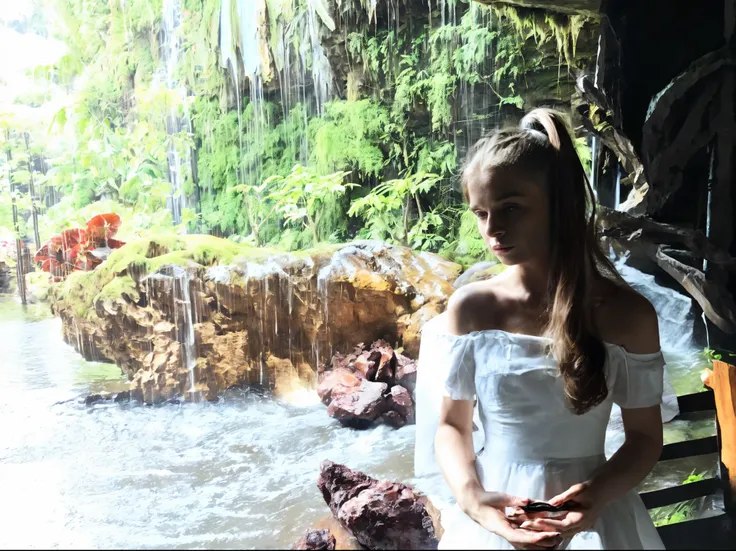 there is a beautiful  woman in a white dress standing by a waterfall, in a cave with the waterfall, next to a waterfall, with a waterfalls, standing near a waterfall, waterfalls in the background,