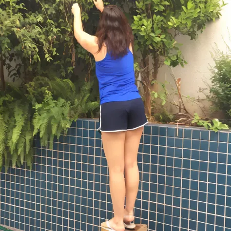 woman in blue shirt and dark blue short shorts and light blue short t-shirt, on a bench next to a garden, shot from behind, back pose, shot from behind, shot from behind, long shot from behind, in shorts, shot from behind , rear - photo, seen from the back...