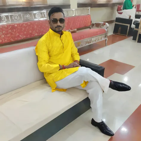 there is a man sitting on a bench in a room, with yellow cloths, wearing a kurta, dressed in a jodhpuri suit, wearing a silk kurta, very very low quality picture, wearing red and yellow clothes, yellow clothes, king in yellow, dressed with long fluent clot...