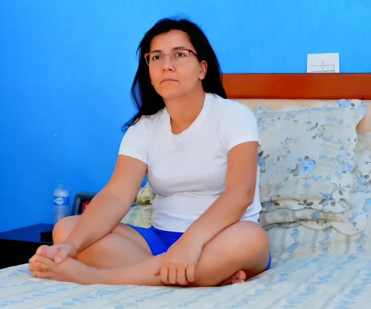 there is a woman sitting on a bed with a blue wall, sitting in bedroom, someone in home sits in bed, sitting on the bed, sitting on a bed, 30-year-old woman from cuba, sitting on the edge of a bed, someone sits in bed, woman is sitting, portrait of a 40 ye...