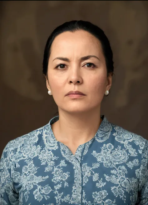 The image is a portrait of a woman with a serious expression. She had black hair and was wearing a blue and white patterned top.