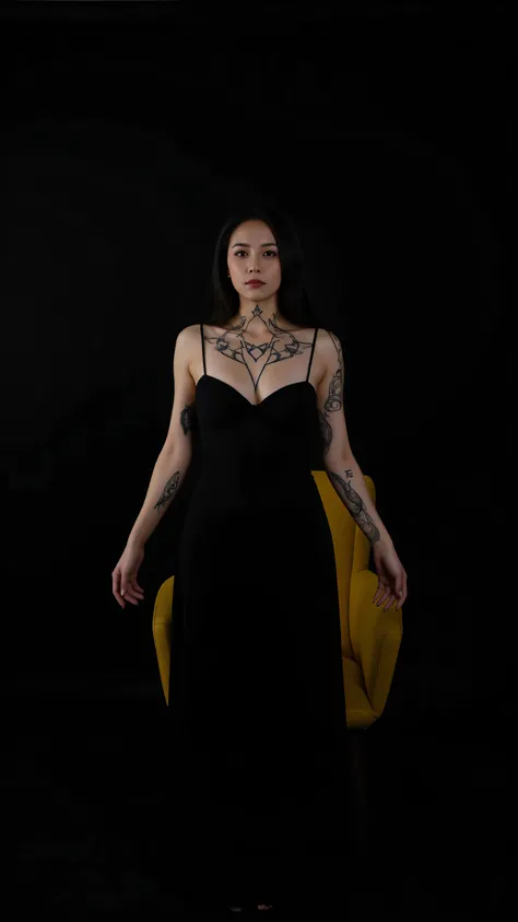 Several tattoos of Wicca symbols on the back of the neck and arms of a woman in a long dress standing in a black studio with a yellow chair 