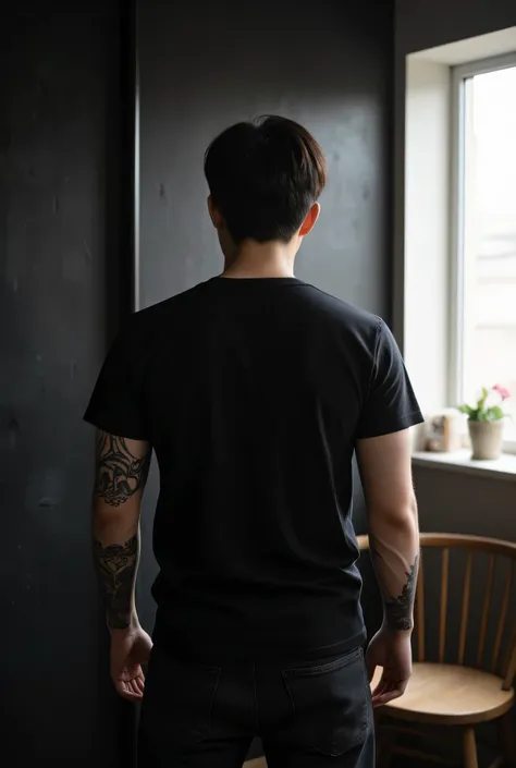 young korean man, wearing plain black t-shirt, wearing black jeans, back view, facing back, hands full of tattoos, dark wall background, bright room.